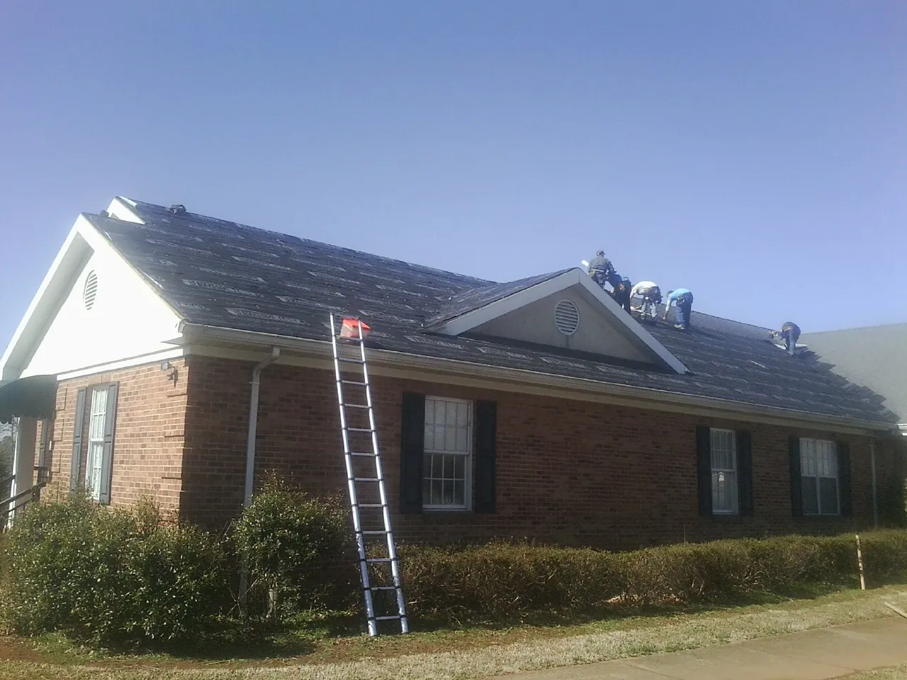 Crew tearing shingles off a brick ranch roof with a ladder set — Emergency Roof Repair work by our crew in Salters