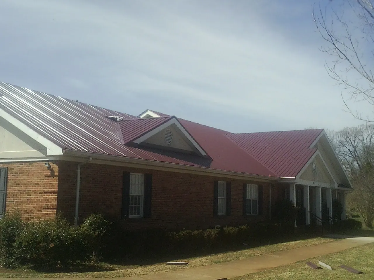Red metal roof with gabled entries on a long brick building, from a Hail Damage Roof Repair job in Salters
