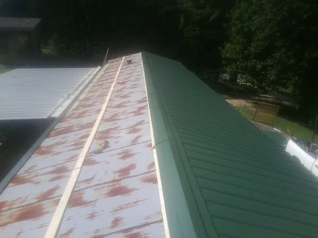 Old rusted panels beside newly installed green metal roofing — Wind Damage Roof Repair by Roofing Brothers in Salters