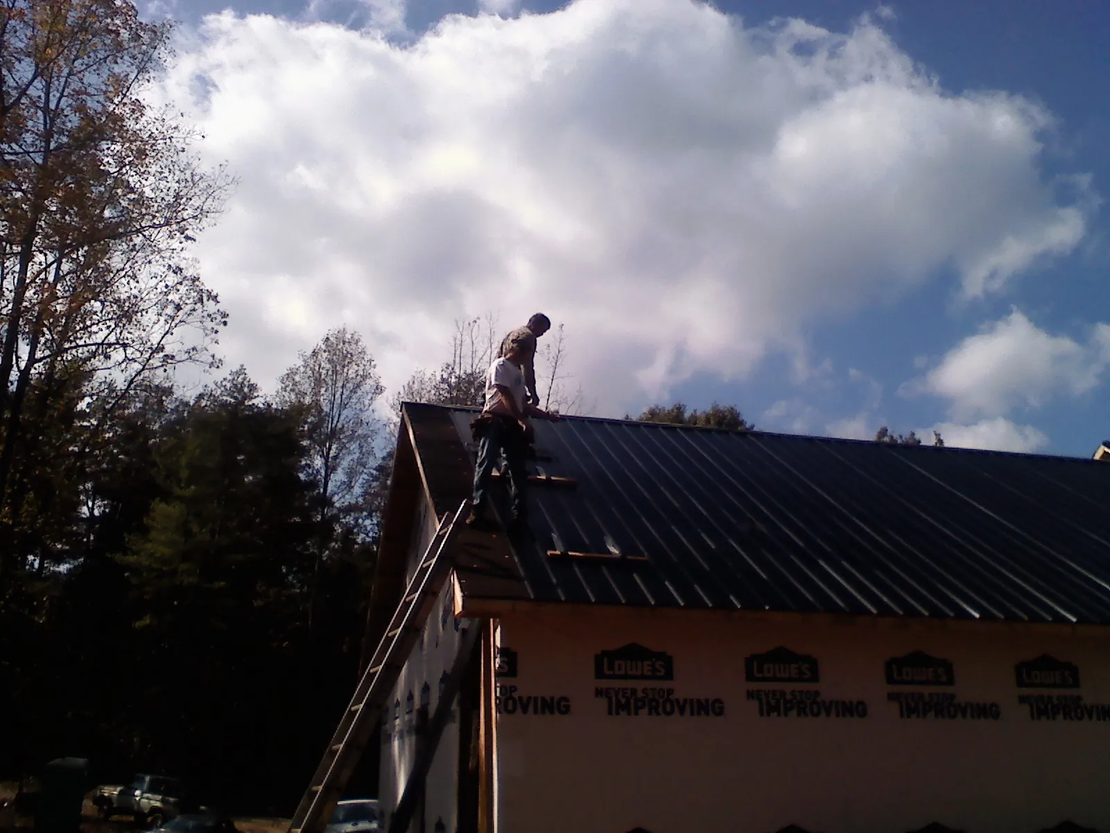 Roofer fastening dark metal panels high against a cloudy sky, from a Roof Inspection job in Salters