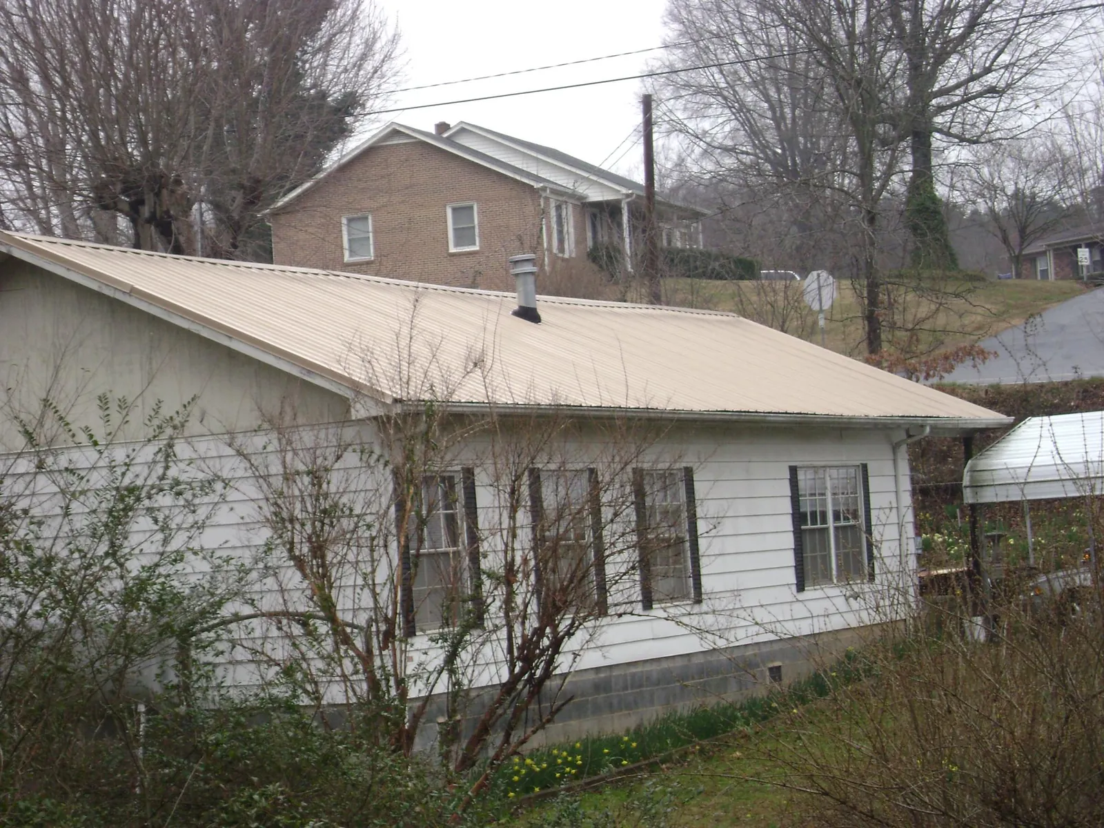 Tan metal roof on a white sided house set into a hillside — Commercial Roofing by Roofing Brothers in Salters